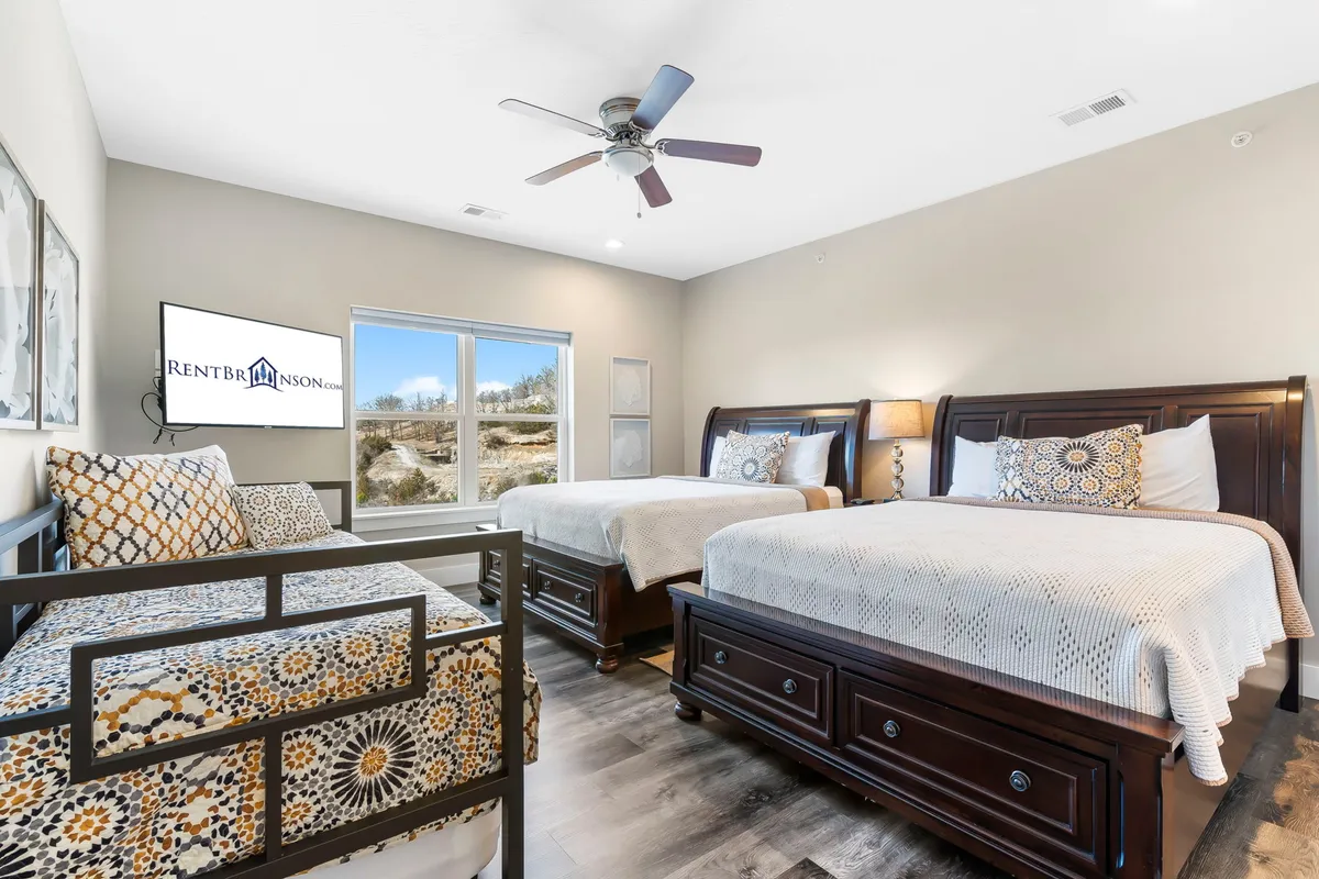A spacious bedroom with two large beds dressed in decorative pillows, and a window that offers a pleasant outside view. The room is well-lit, cozy, and ideal for small families or friends sharing a space, highlighting both comfort and versatility.