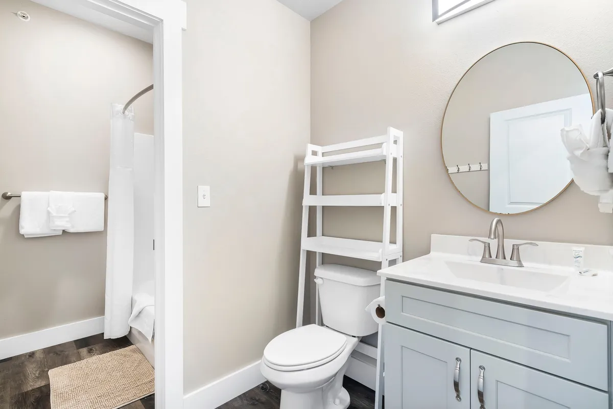 A fresh and inviting ensuite bathroom with a modern vanity, large round mirror, toilet, towel rack, and a shower area. The clean lines and thoughtful details create a spa-like environment, perfect for relaxation and self-care after a day of adventure.