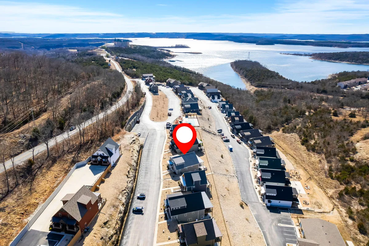 A tranquil exterior scene with newly constructed homes nestled among trees, a winding road, and a beautiful view of the lake in the background. The openness of the landscape suggests ample space for walks, exploration, and outdoor activities.