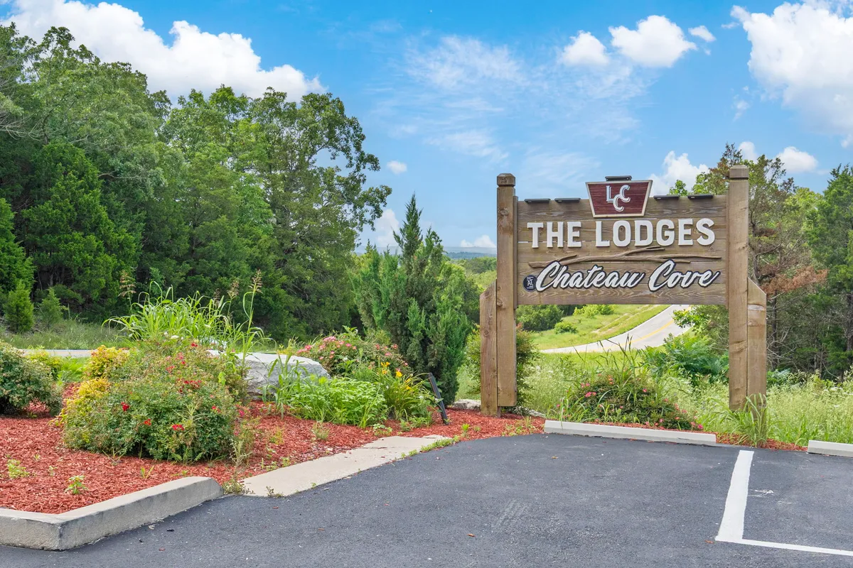 The entrance sign for 'The Lodges at Chateau Cove' is surrounded by landscaped flower beds, trees, and lush greenery. The scene is inviting and shows a well-maintained, welcoming environment right at the doorstep of the property.