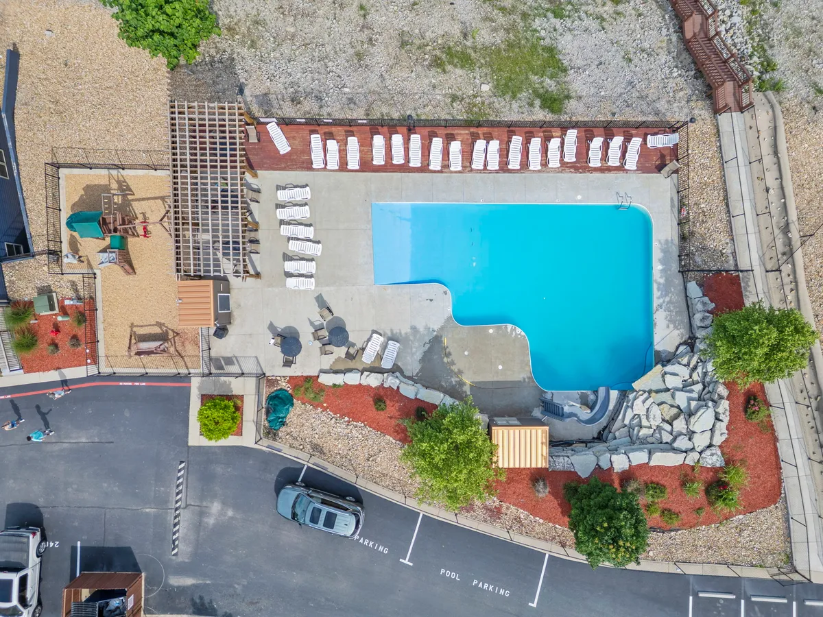 A vibrant exterior shot showing a sparkling swimming pool flanked by lounge chairs and a playground structure, surrounded by landscaped areas. The scene is lively and summery, suggesting joyful family gatherings and poolside relaxation, with the playground hinting at child-friendly recreation.