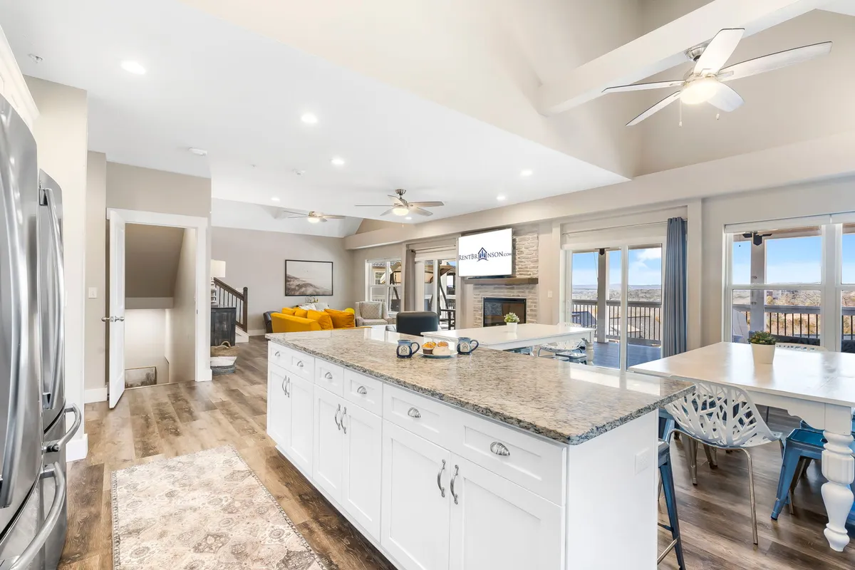 A welcoming view of the main living area, featuring a kitchen island, a vibrant yellow sofa, a stone fireplace, and expansive windows. The open arrangement connects cooking, dining, and relaxing spaces, while the large windows frame the scenic lake, further enhancing the sense of togetherness.