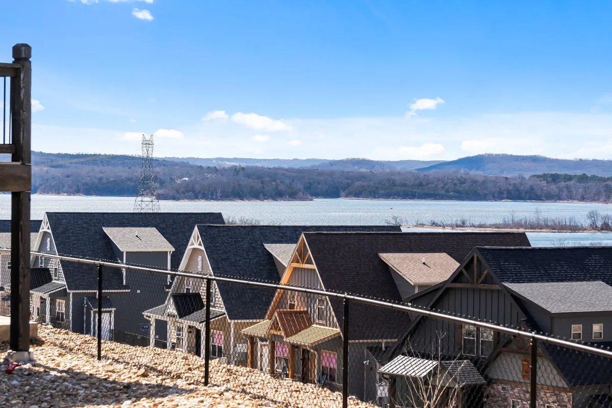This image presents an expansive view looking over the rooftops of homes toward the sparkling Table Rock Lake, with distant mountains and a clear blue sky creating a tranquil, scenic backdrop. The lake’s proximity and natural beauty are center stage, evoking the sense of adventure and relaxation described in the section.