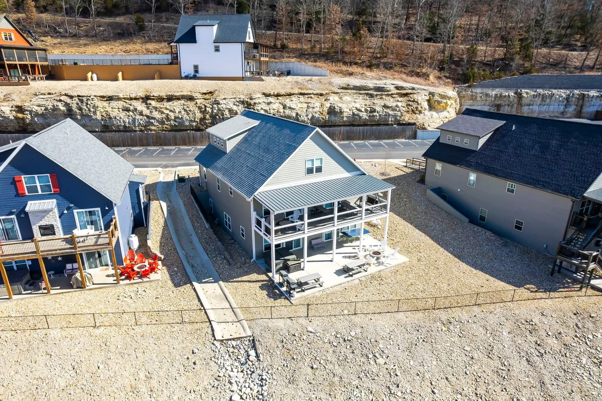 An inviting exterior shot of the main house with a welcoming porch, adjacent homes, and an exposed rock face in the background. The setting feels casual and social, evoking gatherings, barbecues, or evenings spent relaxing outdoors with friends and family.