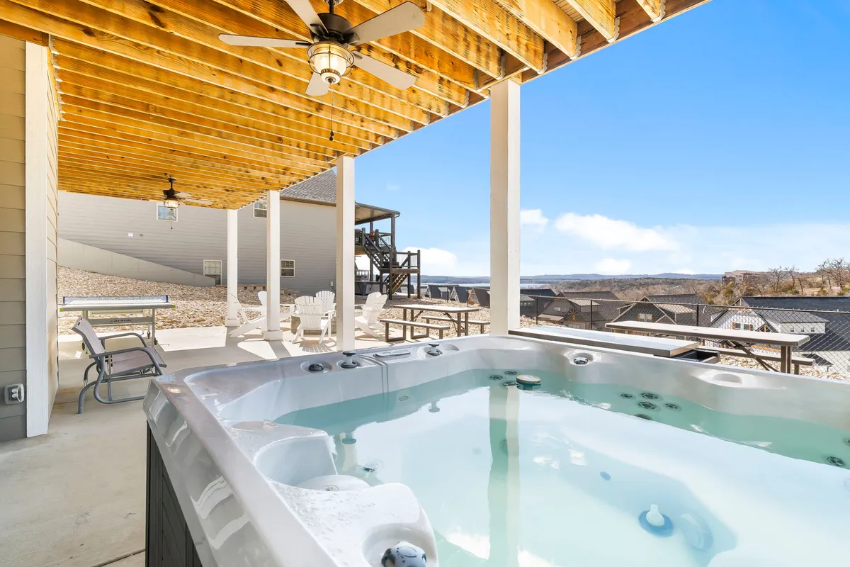 The image showcases the exterior of Lakeview Chateau Lodge, focusing on a bubbling hot tub and inviting outdoor seating area overlooking panoramic mountain and lake views. The scene captures a vibrant sunset, suggesting the perfect setting for relaxation, socializing, and enjoying nature in comfort.